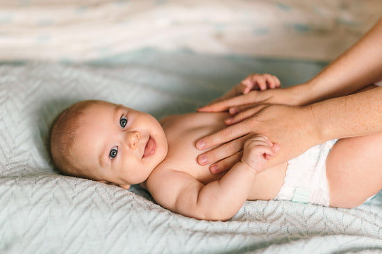 Baby liegt auf dem Bett und wird am Bauch gestreichelt