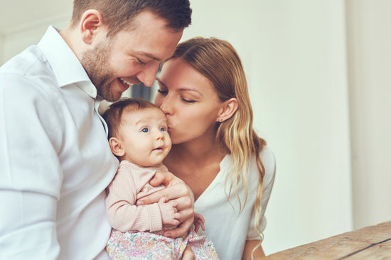 Junge Familie hält Baby im Arm. Die Frau küsst es auf den Kopf.