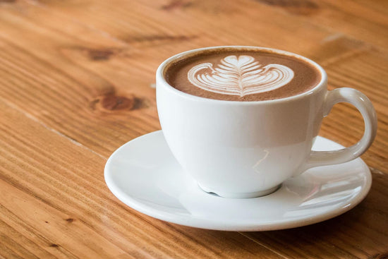 Eine Kaffeetasse mit Latte Art steht auf einem Holztisch.