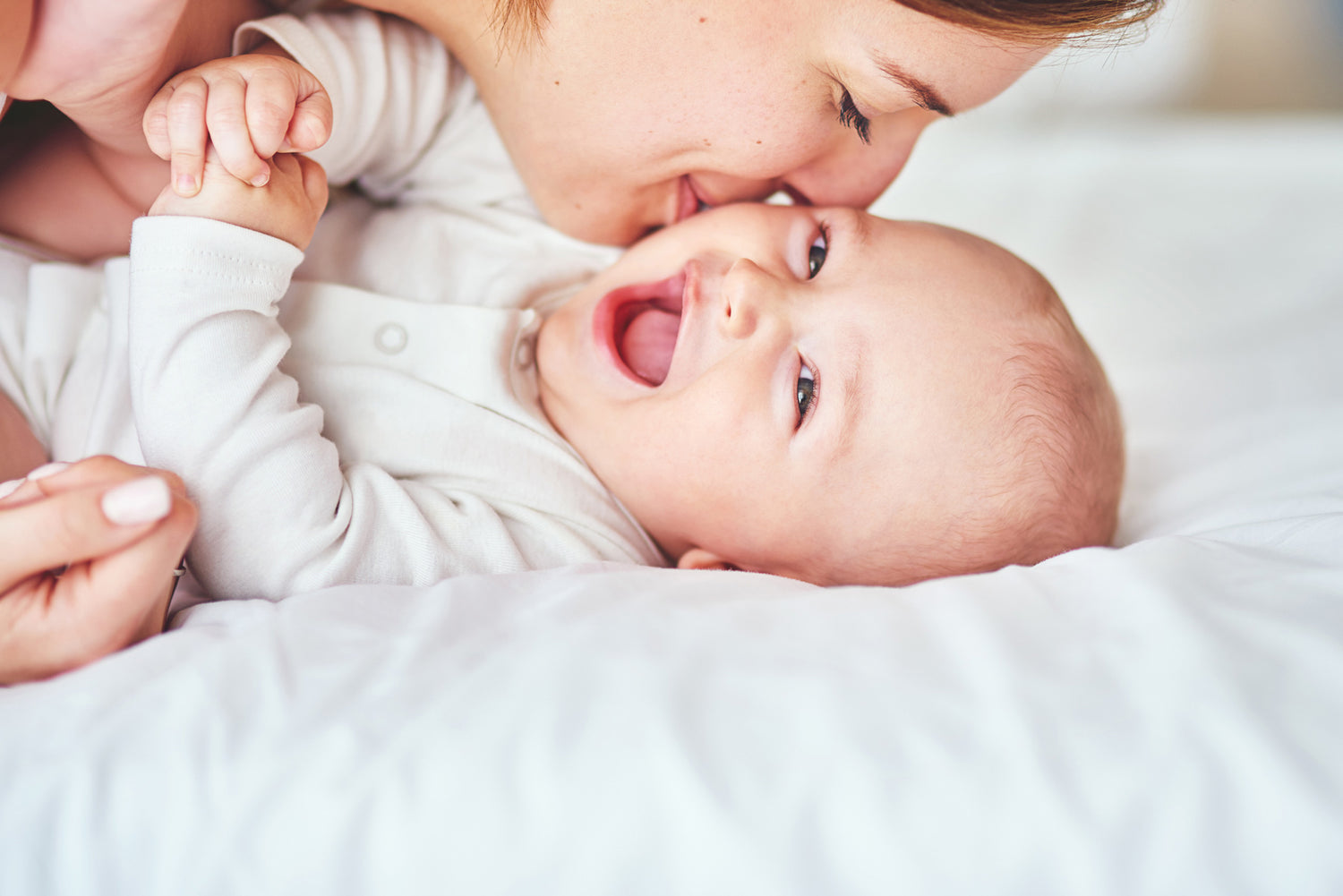 Mutter küsst Baby welches auf dem Bett liegt und lacht