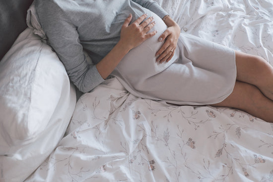 Schwangere Frau liegt auf dem Bett und hält ihren Bauch.