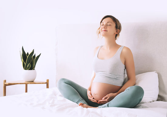 Schwangere Frau sitzt, entspannt und hält ihren Bauch.