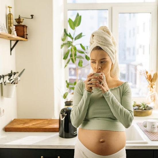 Schwangere Frau in der Küche, die eine Tasse in den Händen vor ihrem Mund hält