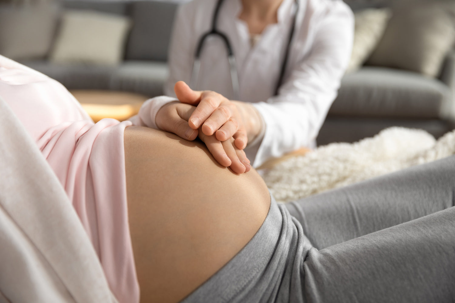 Schwangere Frau ist beim Frauenarzt. Beide Hände liegen auf dem Bauch.