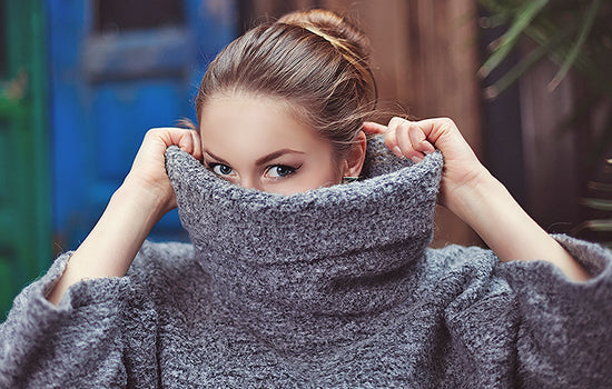 Dunkelblonde Frau zieht Wollpulli über Gesicht
